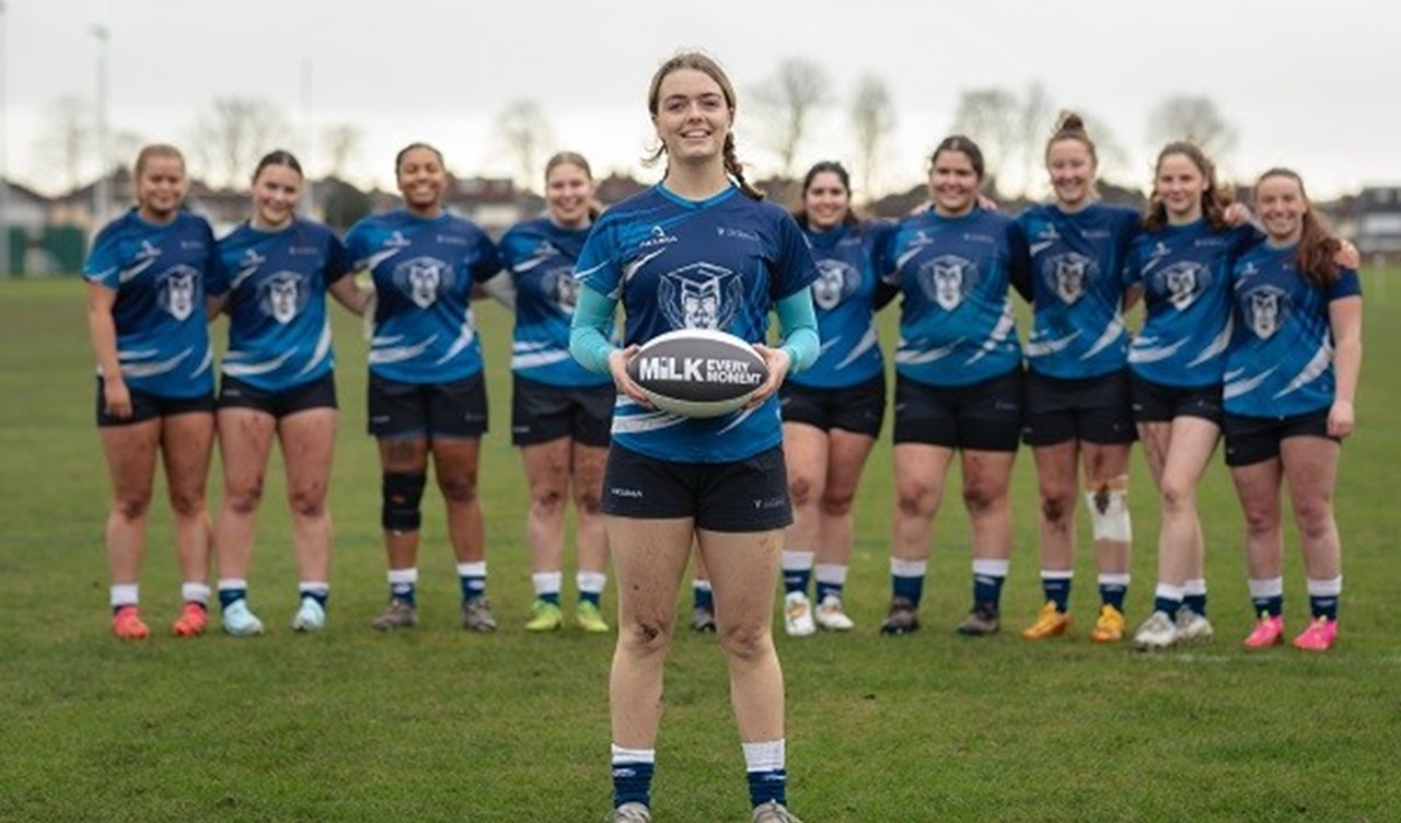 A girl holding a rugby ball with the rest of the team standing behind her.